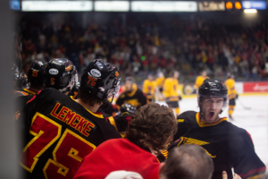 #75 Justin Lemcke celebrates a goal with his teammates from the bench as they skate by.