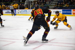 #43 winds up for a shot against Laurier's net with one defender scrambling to stop him.